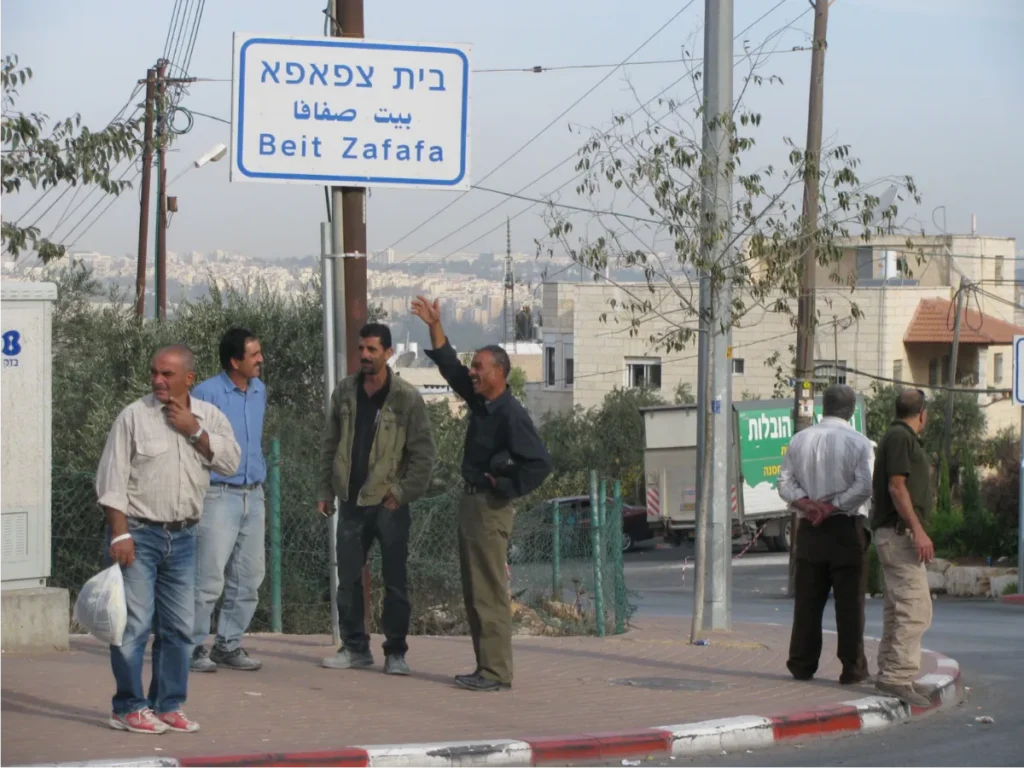 Group of men talking on a street corner beneath a Beit Zafafa street sign